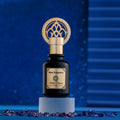 Black bottle gold cap oriental perfume Imperium by Khalifi Perfumes on a blue wooden rounded piece of wood, with sapphires on a blue floor and with a sparkly blue background